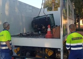 Dos operarios municipales retiran uno de los contenedores quemados la pasada madrugada en La Palma.