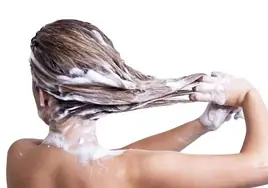 Una mujer se aplica champú en el cabello.