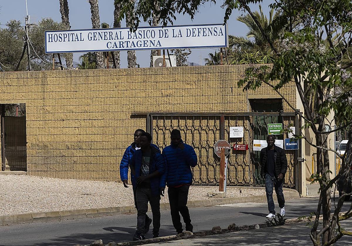 Cuatro inmigrantes salen del campamento del Hospital Naval a donde entra un coche, en una foto del pasado jueves.