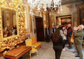 La guía explica a los turistas el contenido del salón amarillo, presidido por un gran espejo.