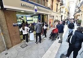 Varias personas hacen cola para adquirir un décimo de la Lotería de Navidad en la administración El Gato Negro en Murcia.