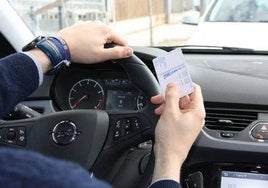 Una persona al volante con el carné de conducir en la mano.