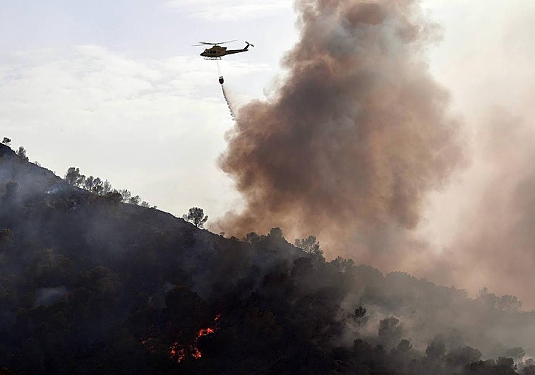 Uno de los tres helicópteros que han intervenido descarga agua sobre las llamas.