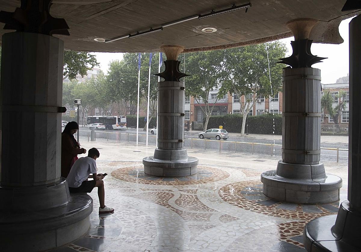 Dos vecinos de Cartagena se resguardan de la lluvia bajo los soportales de la Asamblea Regional
