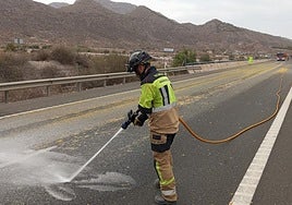 Un bombero limpia la calzada, tras la caída del cargamento de naranjas.