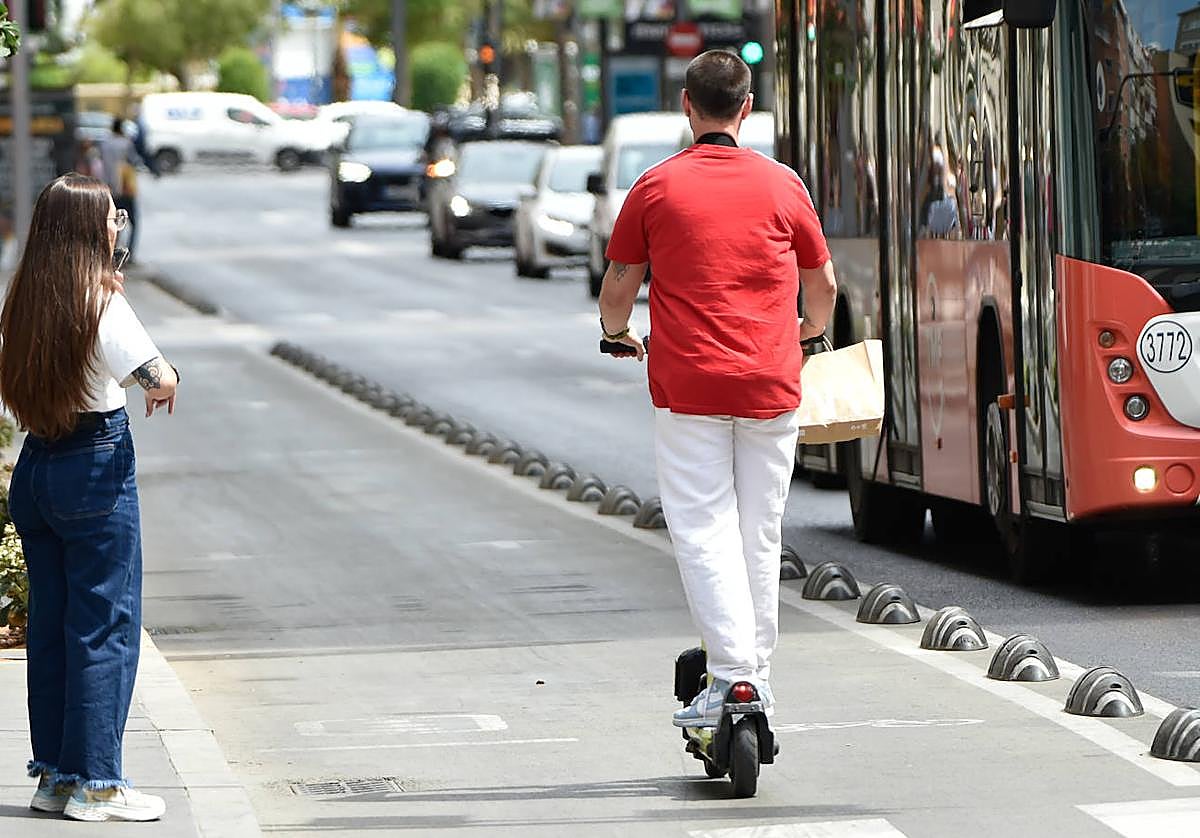 Un hombre circula en patinete por el carril bici en paralelo a un autobús.