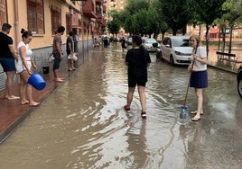 Los vecinos de la calle tratan de bajar el nivel de agua de la calle tras limpiar los imbornales el pasado 12 de junio tras las lluvias torrenciales.