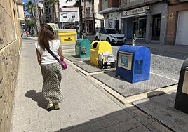 Una vecina pasa junto a unos contenedores en el centro de Cieza, con cartones depositados fuera.