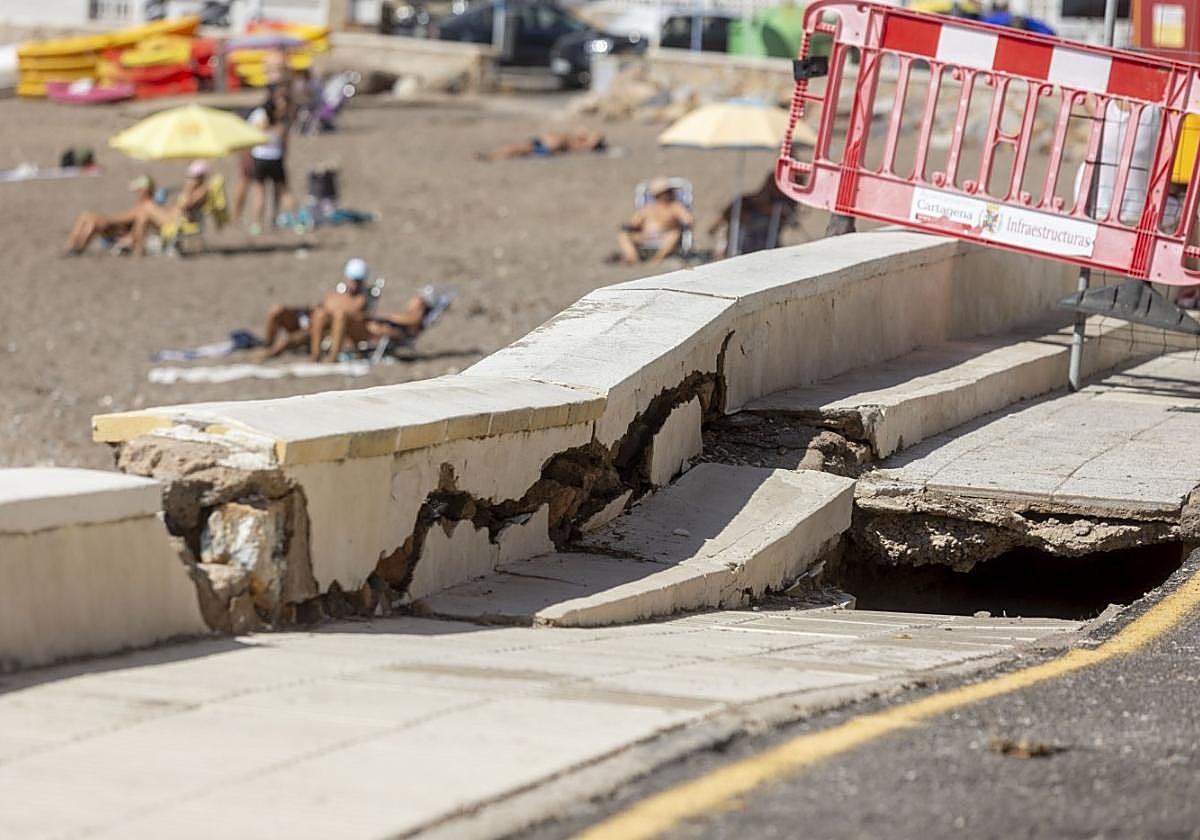 Hundimiento del paseo marítimo de El Portús señalizado, con bañistas al fondo.