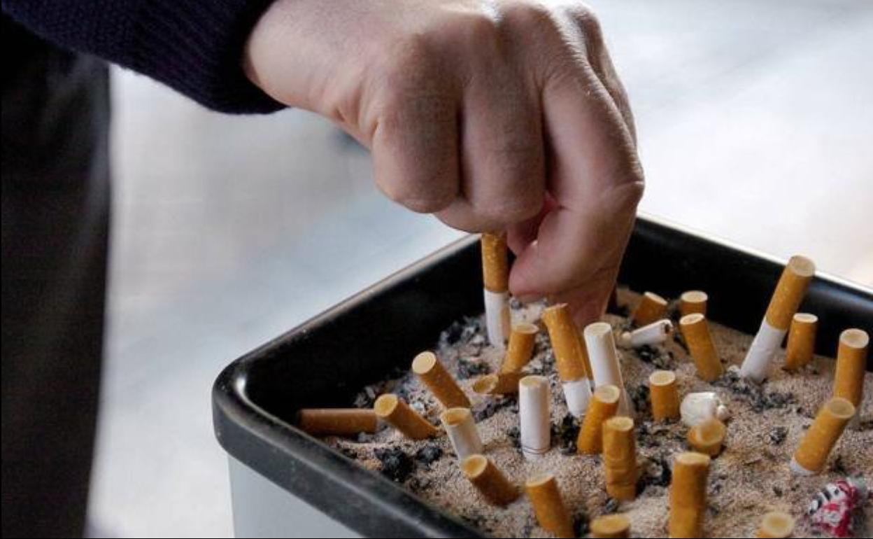 Un hombre apaga un cigarrillo en un cenicero público.