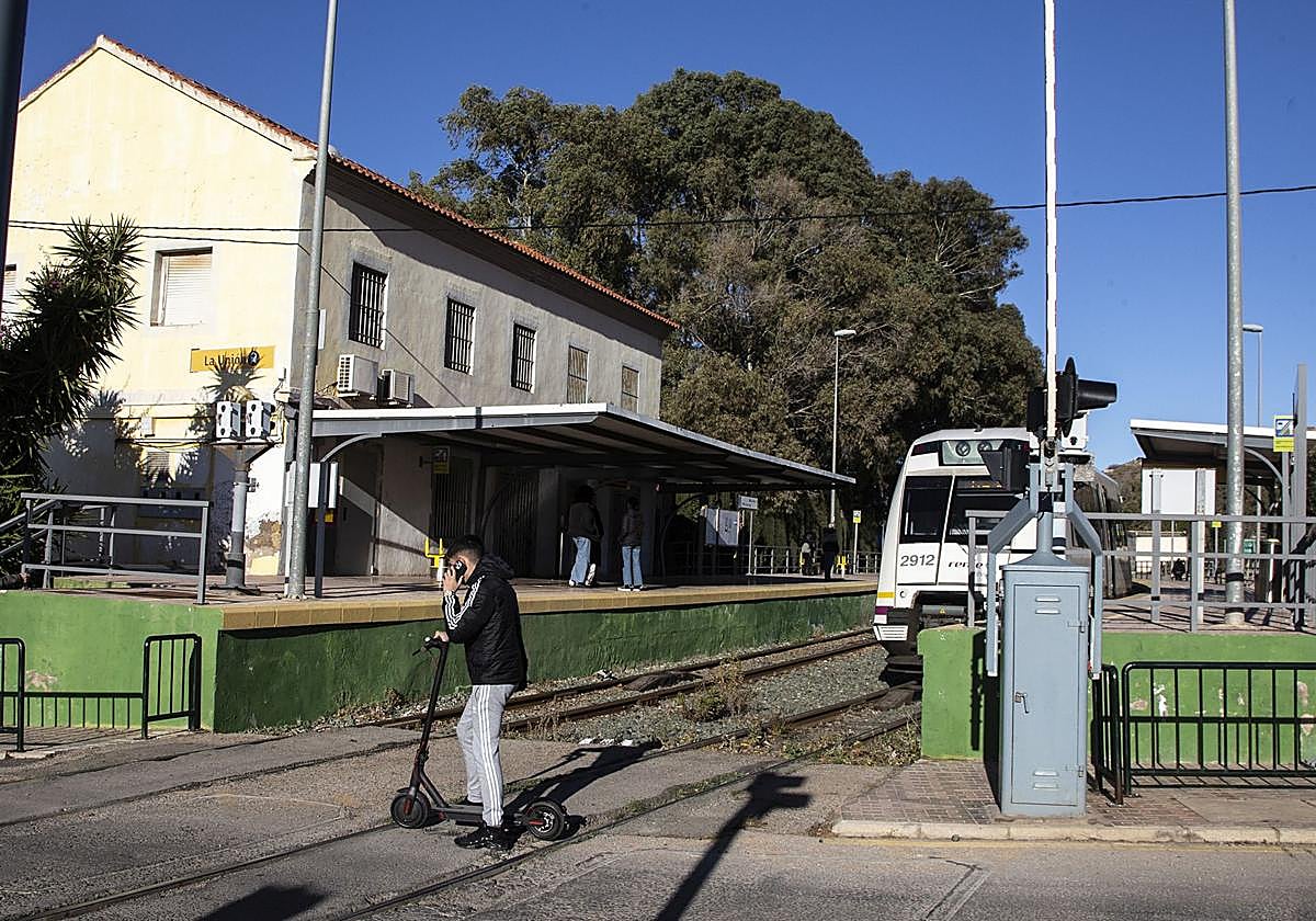 Un joven en patín cruza las vías del Feve en la estación de La Unión, mientras un automotor aguarda el momento de reiniciar la marcha.