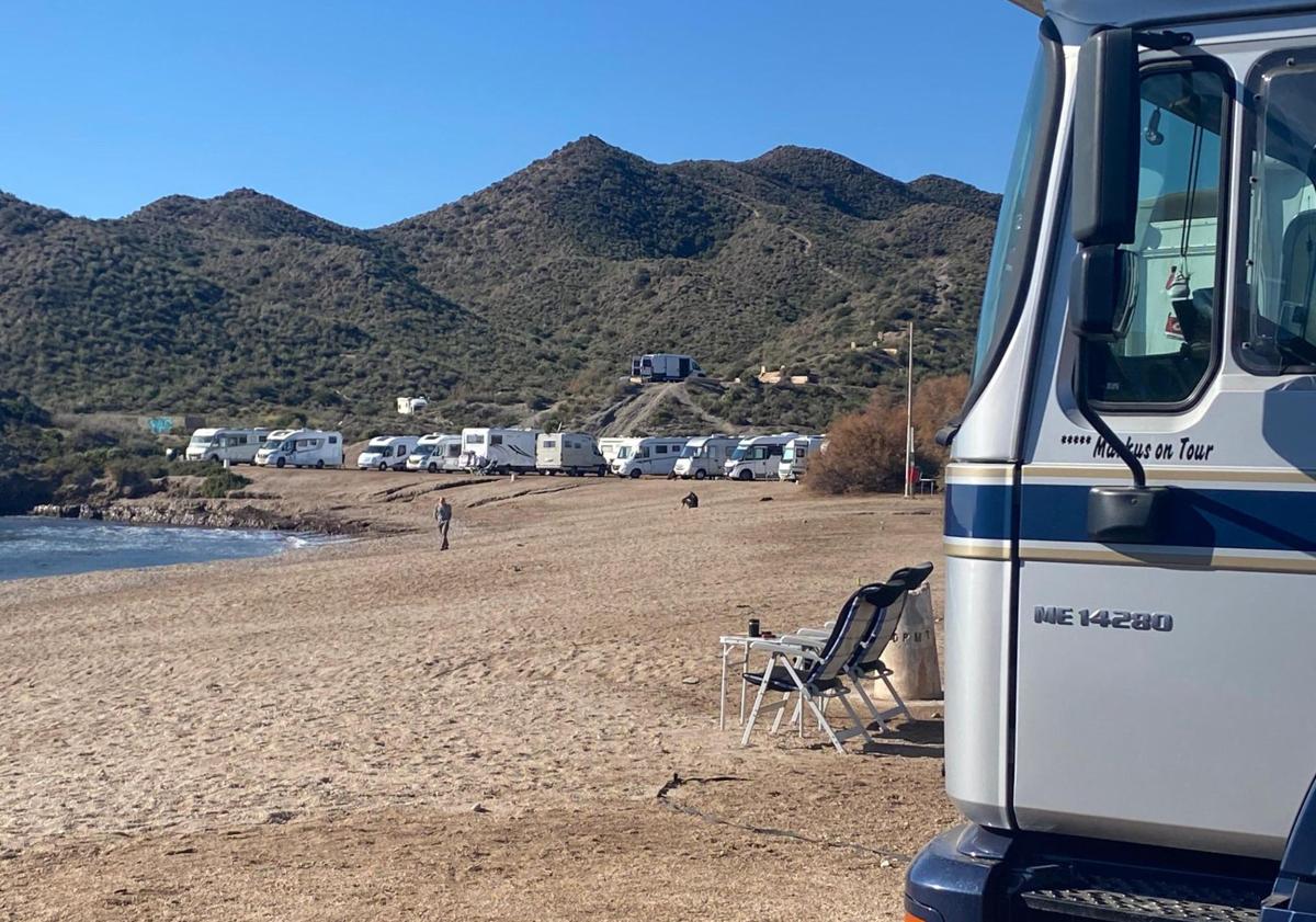 Imagen principal - Autocaravanas instaladas al borde de la playa del Arroz y en sus inmediaciones, con elementos desplegados como sillas y tumbonas. El propietario de una autocaravana transporta un depósito del váter químico que acaba de vaciar junto al cartel de la playa del Arroz, que prohíbe expresamente acampar y aparcar.