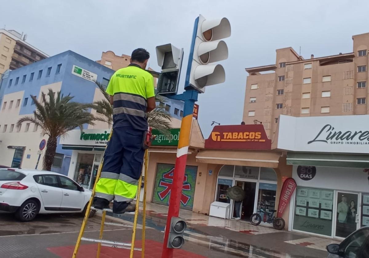 Un técnico de Murtrafic subido a una escalera arregla un semáforo en la Gran Vía de La Manga.