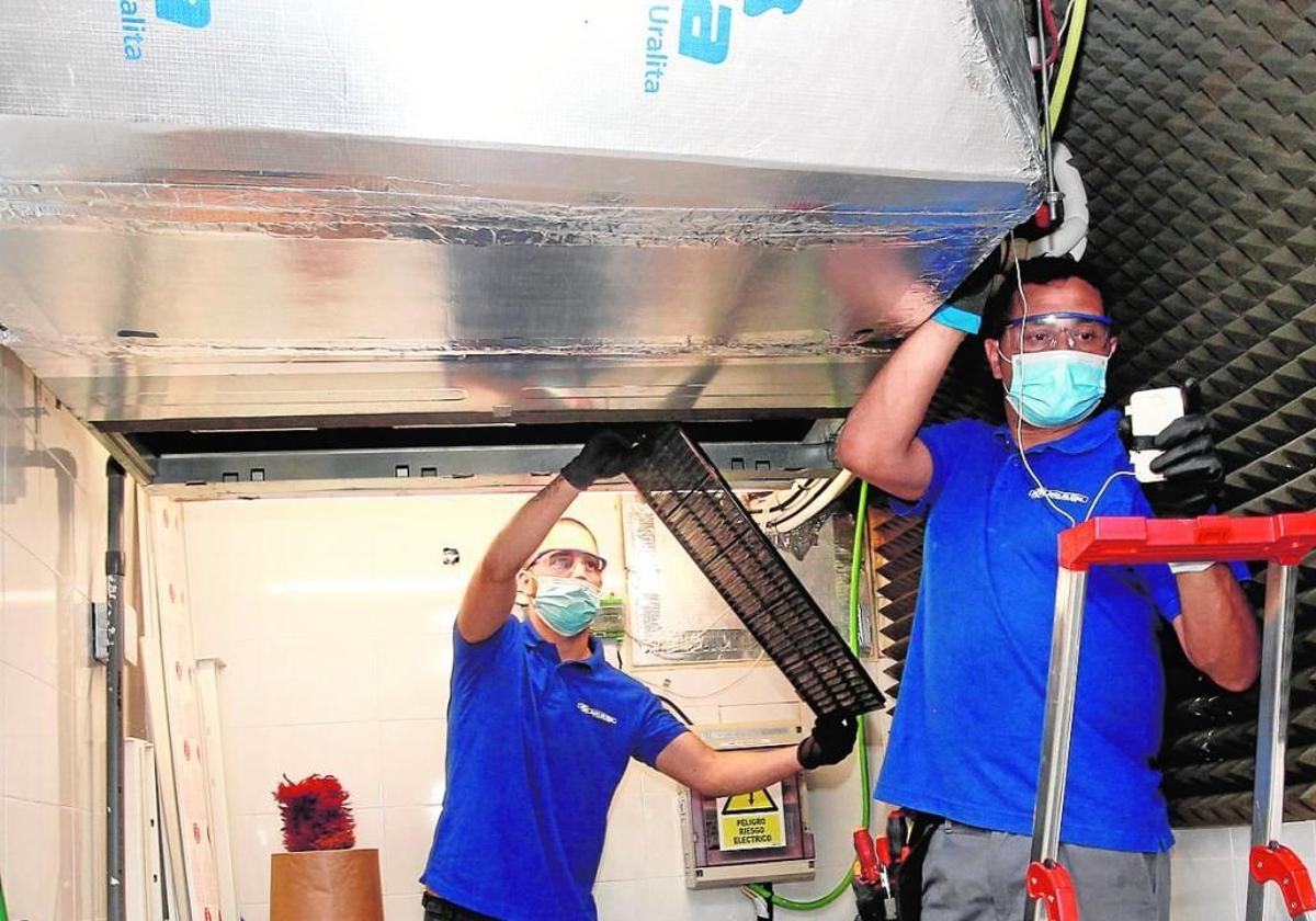 Dos trabajadores revisan aparatos de climatización en un edificio en Murcia.