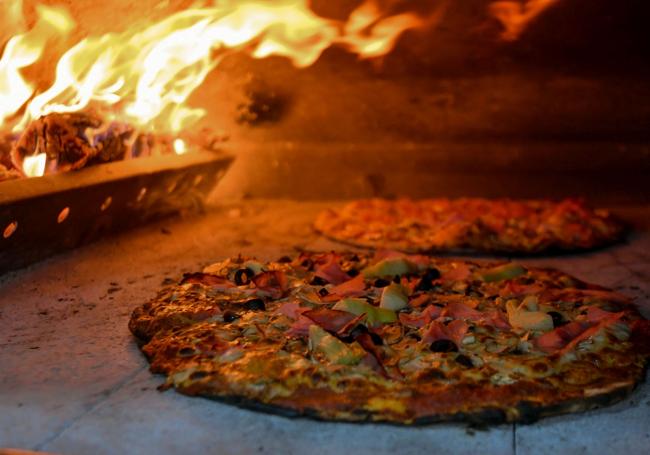 Un par de pizzas cociéndose en el fuego del horno de piedra.