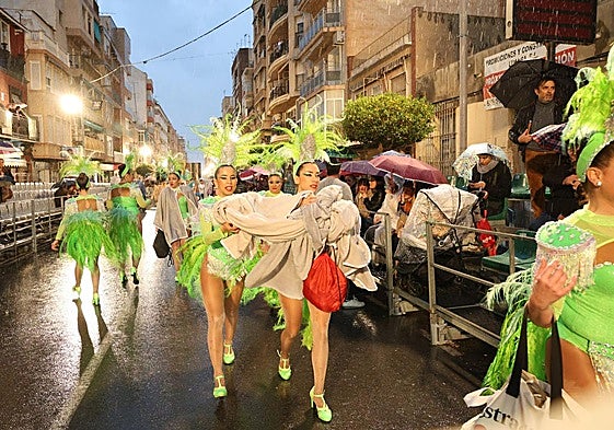 Participantes en el desfile se protegen de la lluvia, este sábado por la tarde.