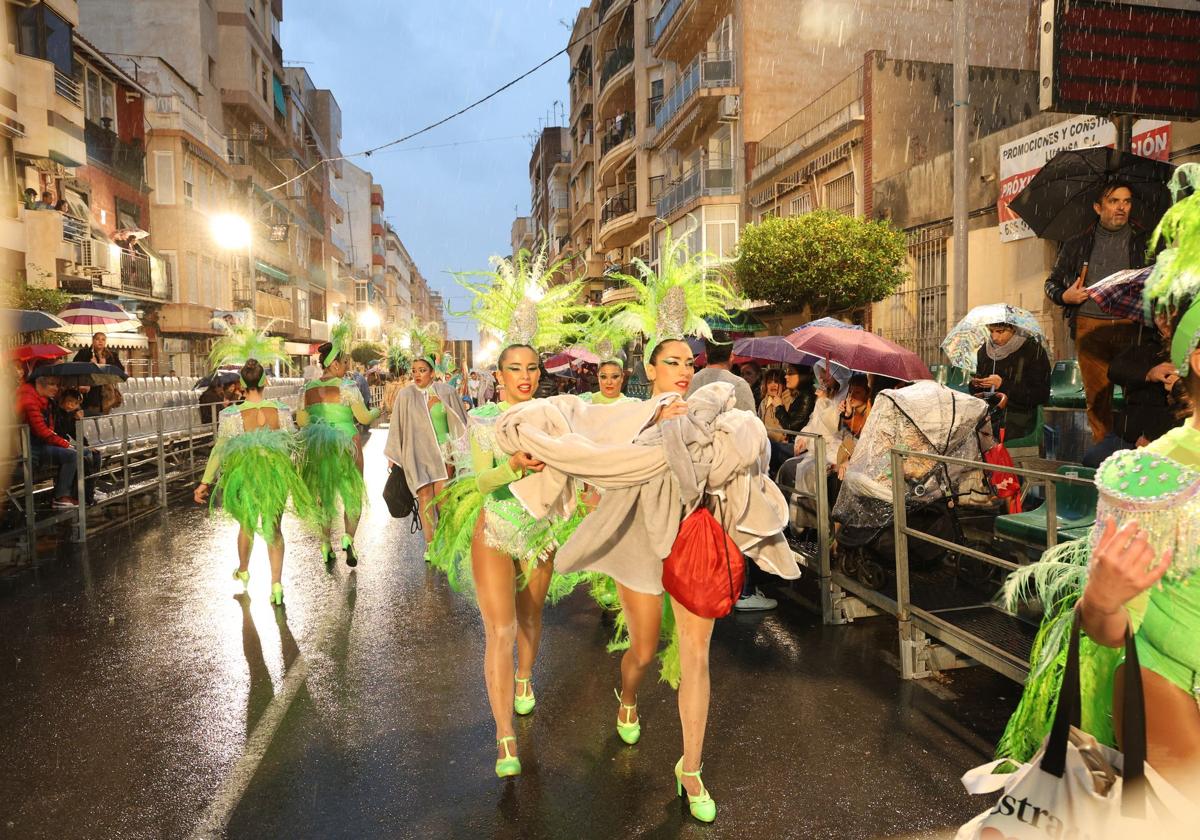 Participantes en el desfile se protegen de la lluvia, este sábado por la tarde.