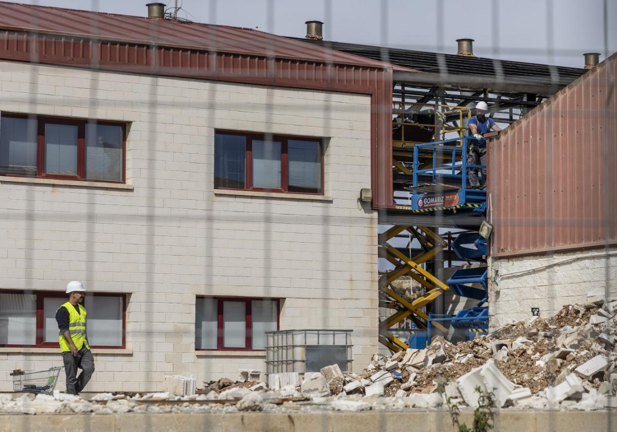 Dos obreros trabajan en el desmontaje y derribo del edificio de talleres portuarios.