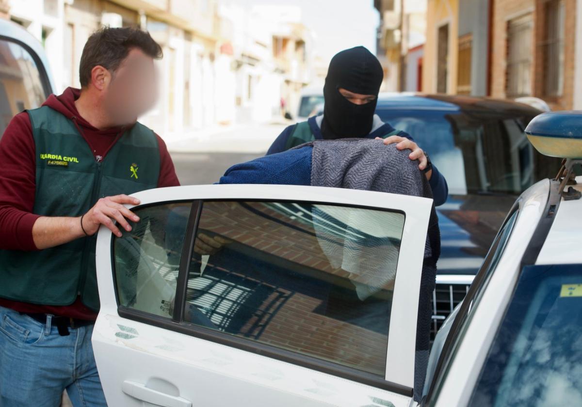 Dos agentes meten en un coche policial a uno de los detenidos en la 'operación Game Rol', en Torre Pacheco.