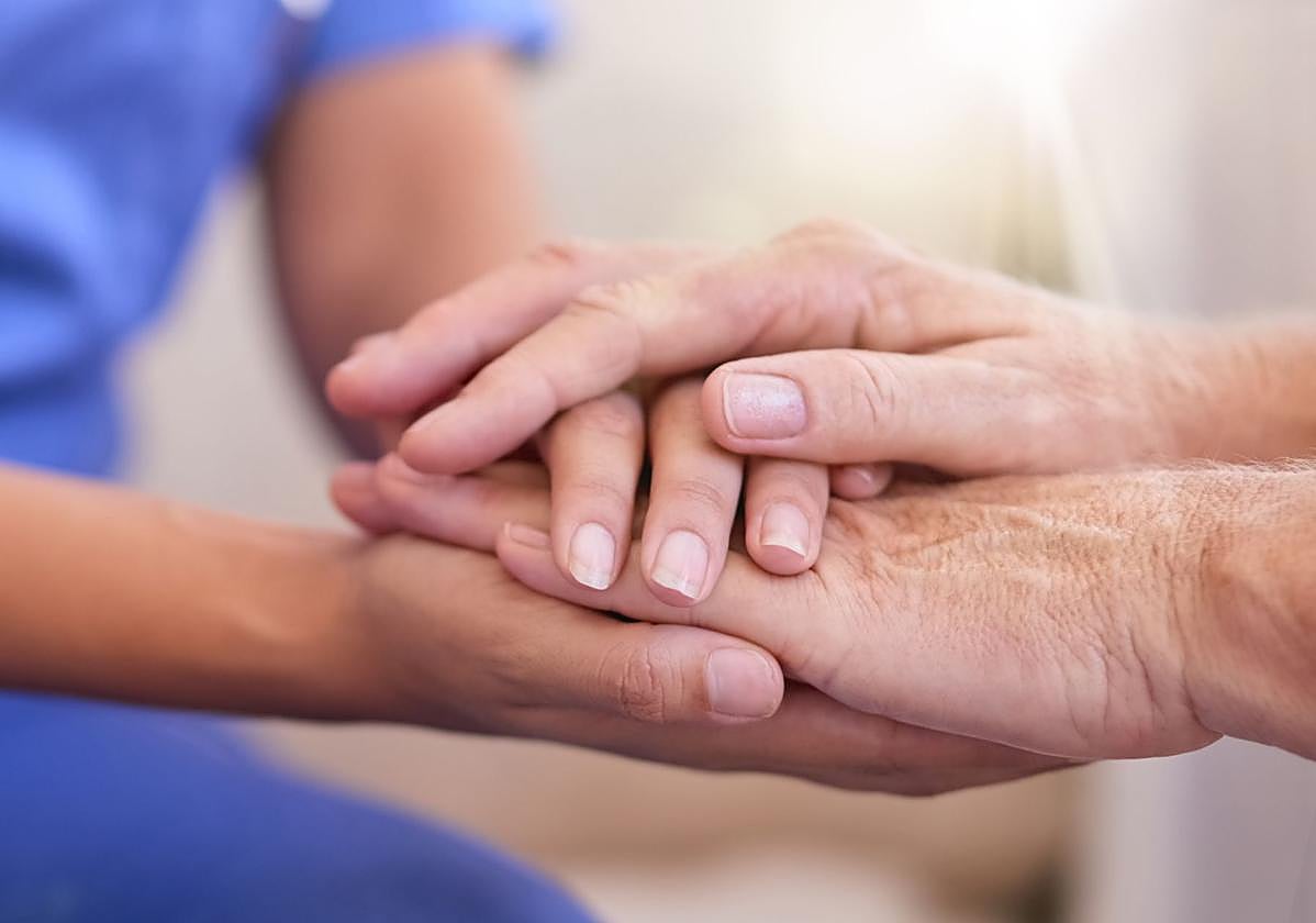 Una enfermera y una paciente juntan sus manos.