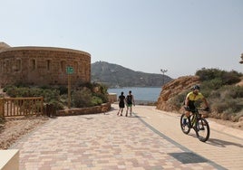 Una pareja, su perro y un ciclista pasean por la senda peatonal que atraviesa algunas baterías de costa camino de Cala Cortina.