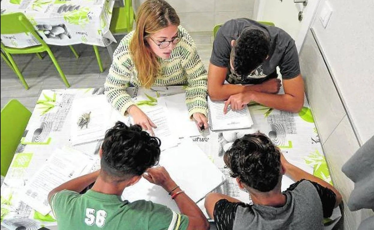 Tres menores del centro Rosa Peñas de la pedanía murciana de Santa Cruz hacen los deberes junto a una de las educadoras, en una imagen de archivo.