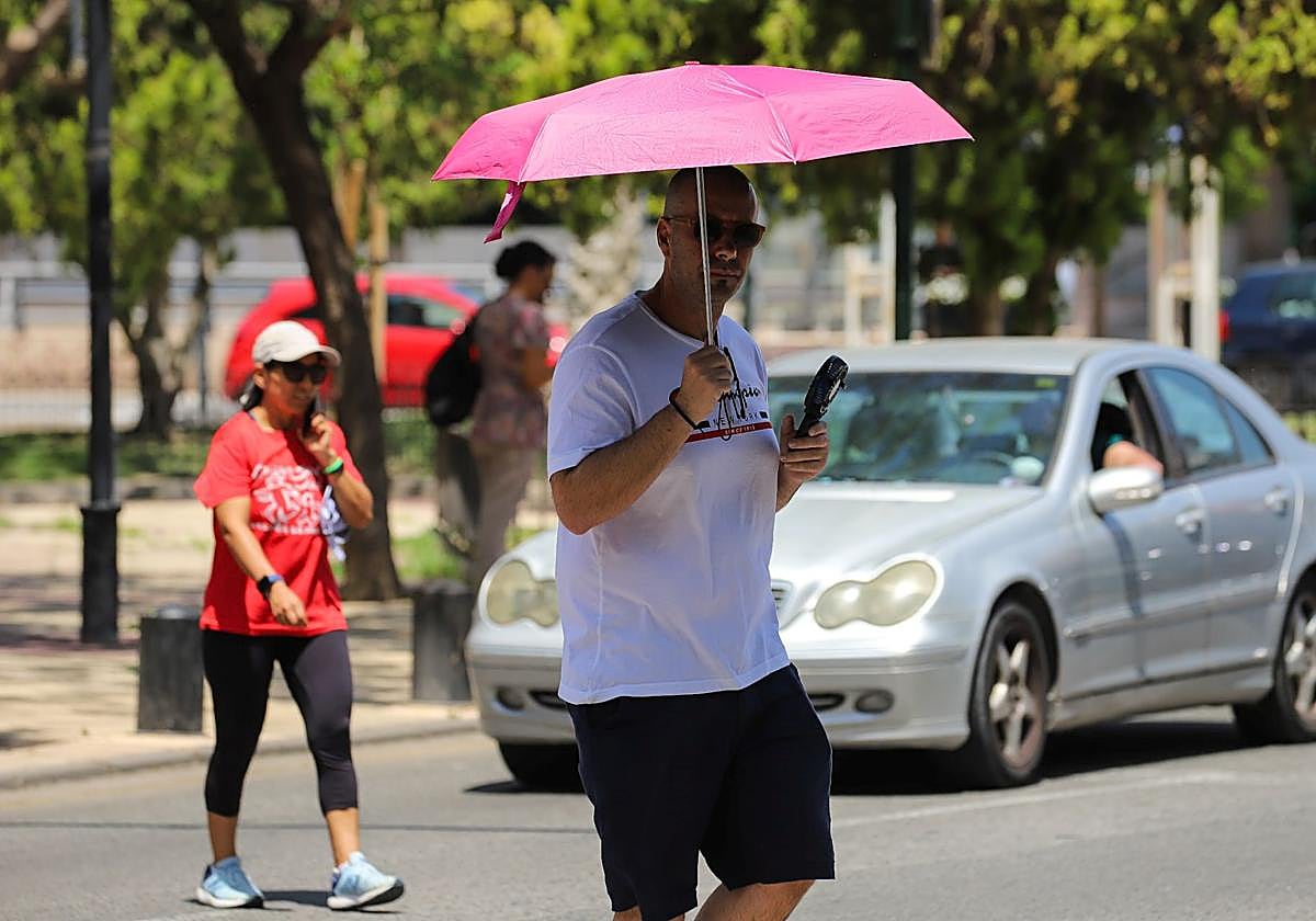 Peatones cruzan una calle en Murcia resguardándose del sol.