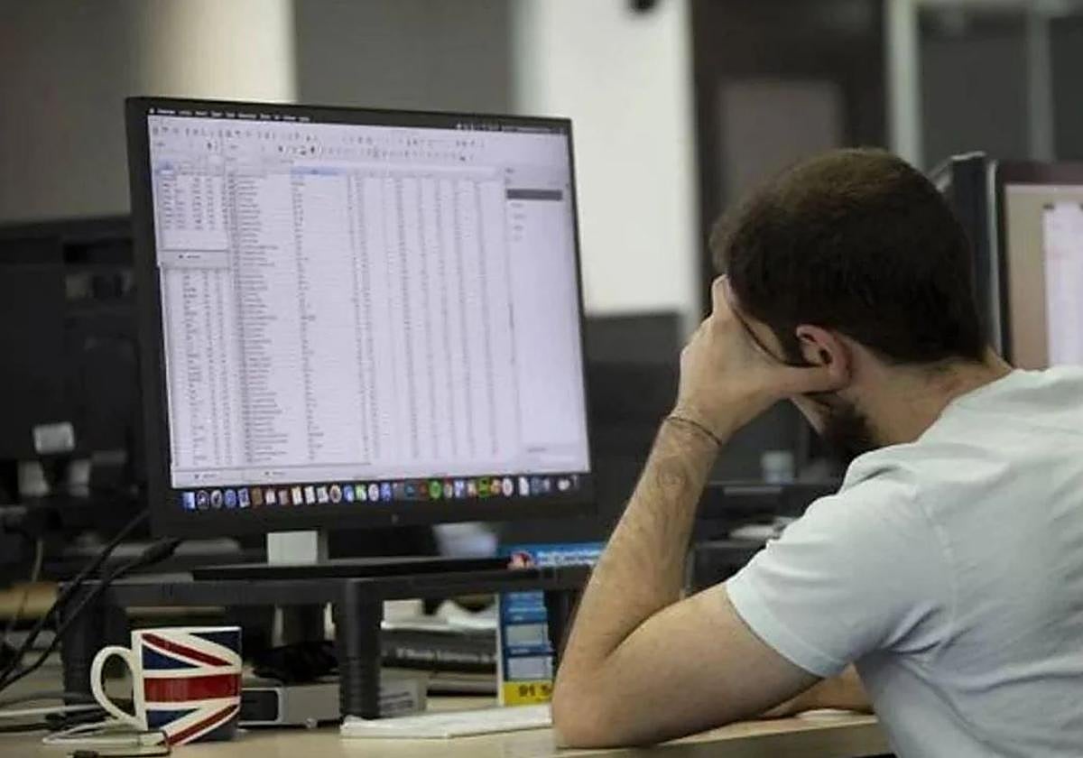 Un trabajador mira con actitud cansada una pantalla de ordenador en una oficina.