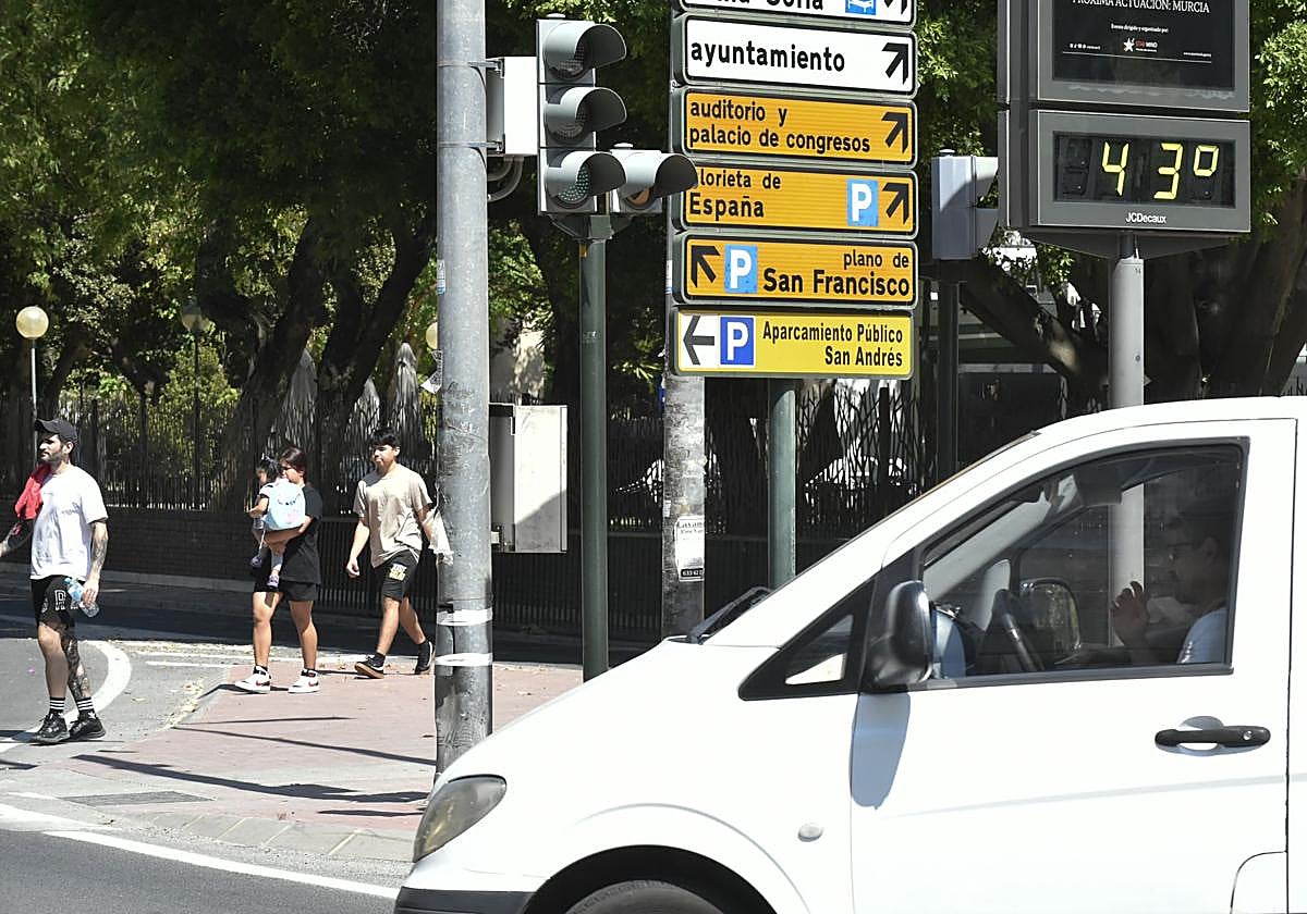 Varios peatones cruzan la calle junto a un termómetro que marca 43 grados.