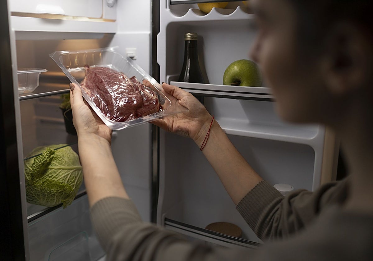 Una mujer guarda una pieza de carne en el frigorífico.