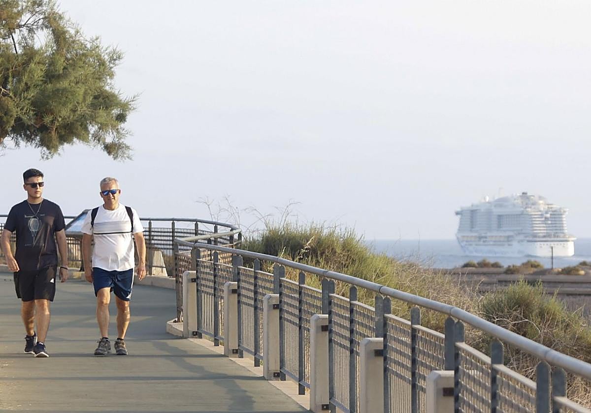 Dos personas caminan por el sendero que comunica las baterías de costa mientras, al fondo, un crucero abandona la bahía.