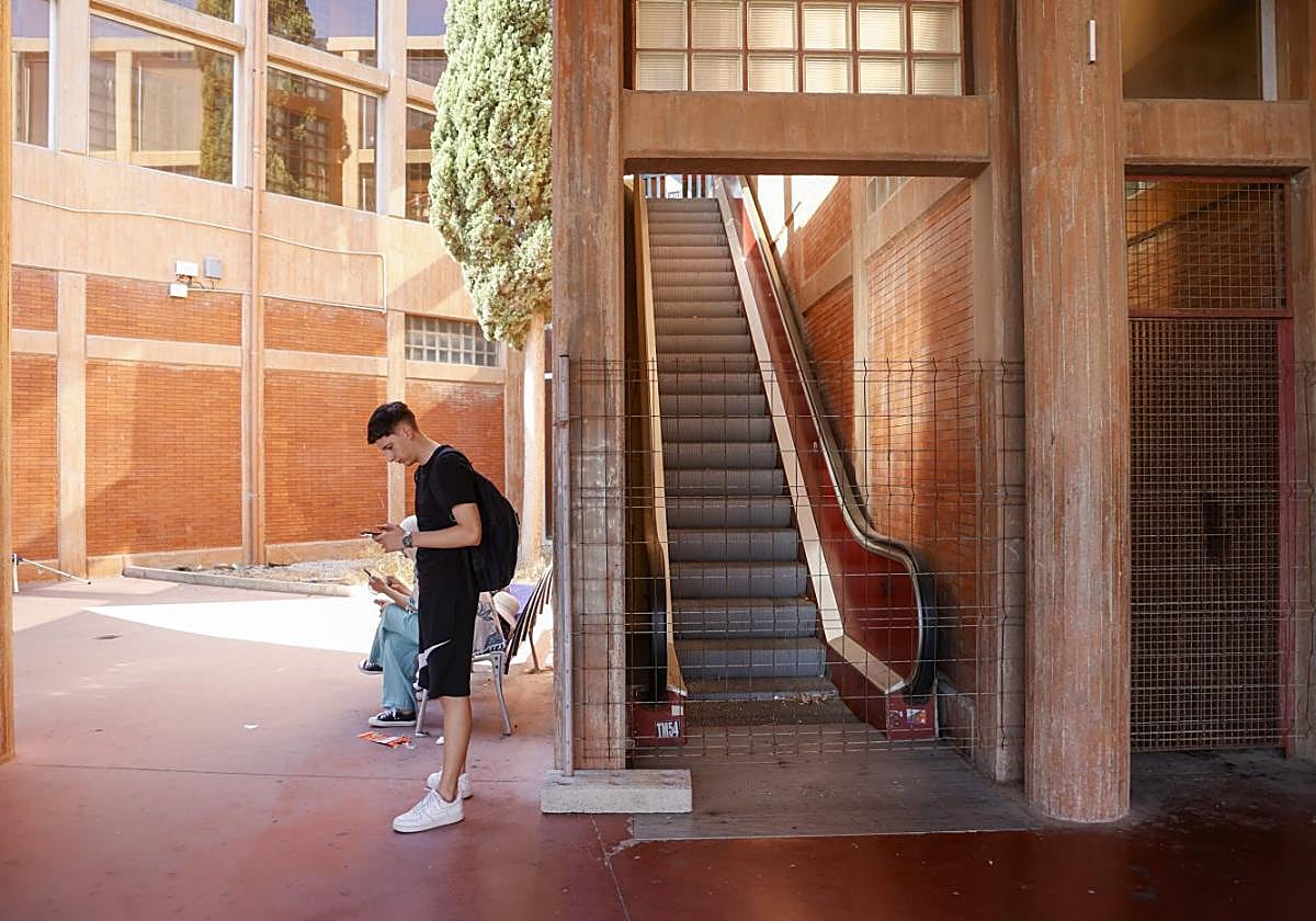 Un viajero hace tiempo en la playa de andenes, junto a unas escaleras mecánicas averiadas y precintadas.