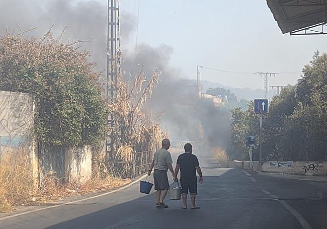 Vecinos cargan con cubos de agua muy cerca del origen del incendio.