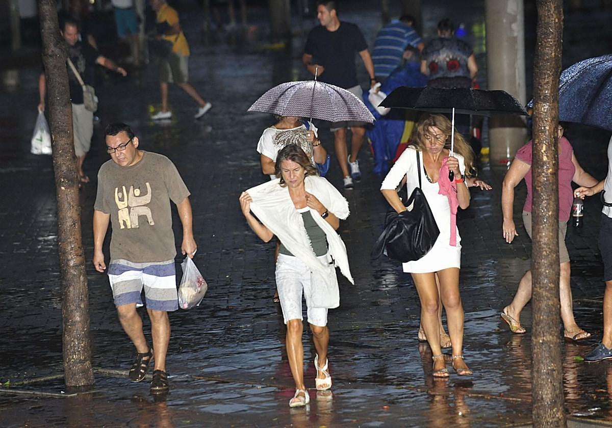 Vecinos de Murcia transitan bajo la lluvia durante una tormenta de verano.