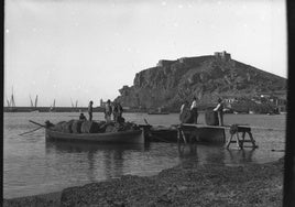 Esparto. Hombres cargando una barca con esparto en la bahía de Águilas. Al fondo, el castillo de San Juan y el puerto de la localidad. (1897).