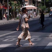 Una mujer cruza un paso de peatones mientras se protege del sol con una sombrilla.