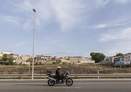 Un policía local circula con su moto por la carretera de La Unión, junto al solar municipal contaminado de Los Mateos.