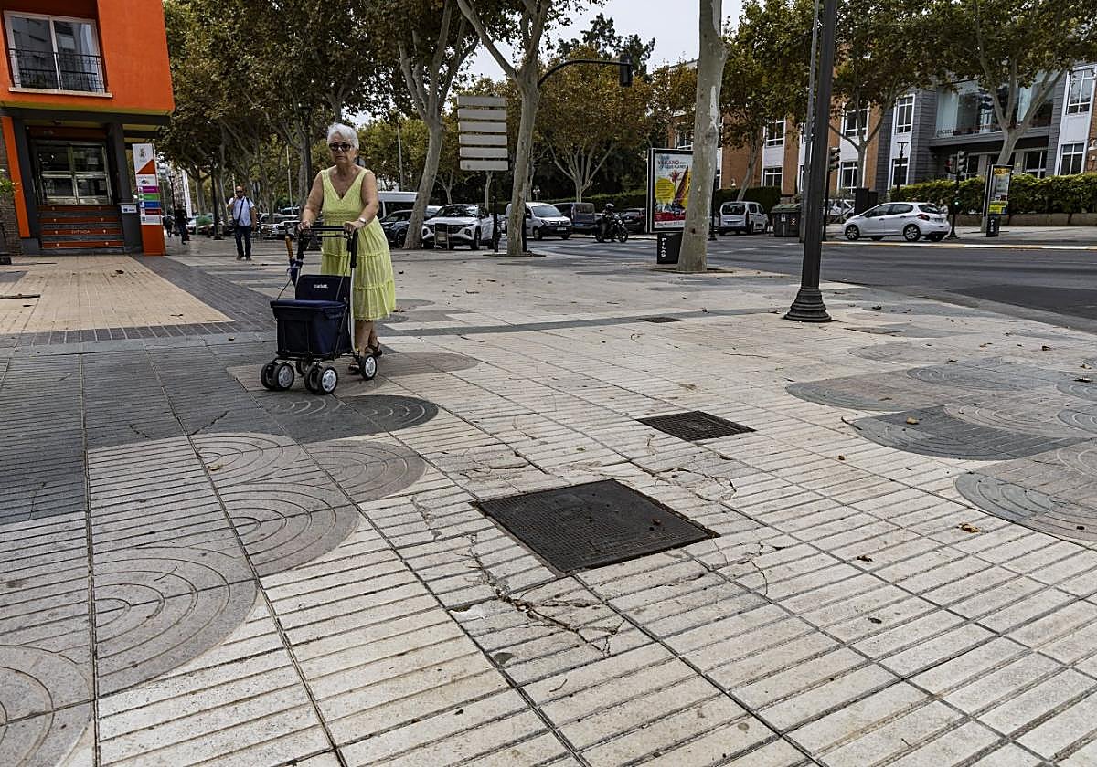 Una mujer camina por el paseo con la ayuda de su andador, rodeada de los desperfectos que hay en las aceras de esta céntrica calle.