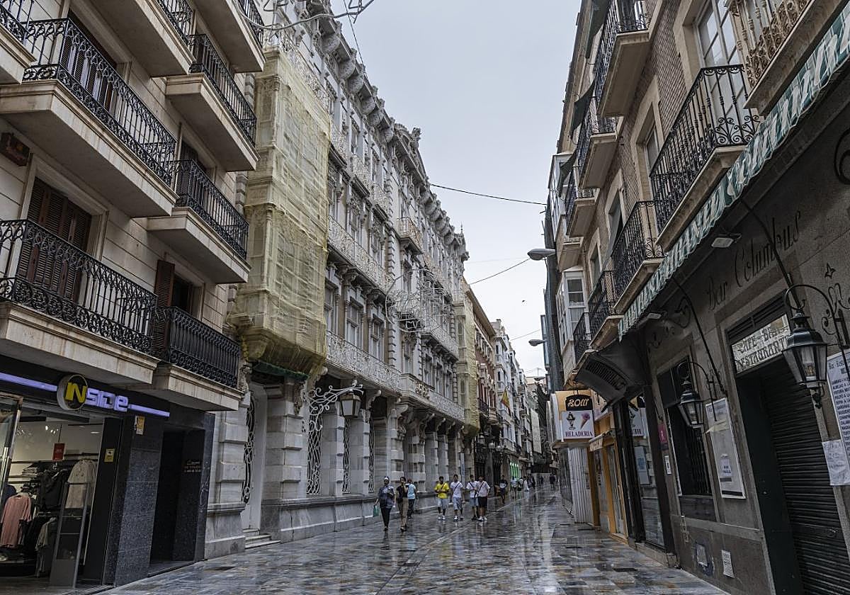 Cartageneros y turistas caminan frente a la fachada de la Casa Cervantes, con sus miradores tapados con mallas amarillas.