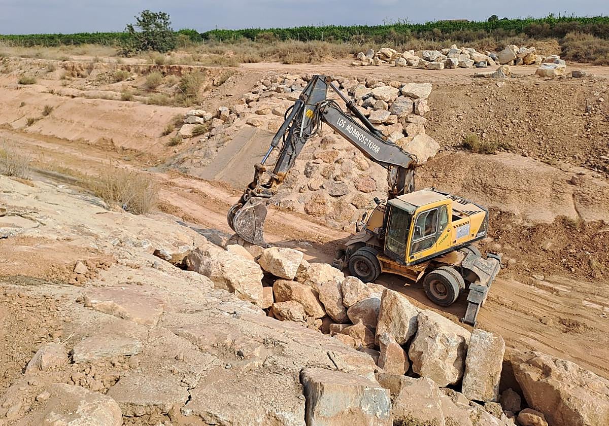 Una excavadora levanta una pared de escollera en el último tramo del cauce de la rambla.