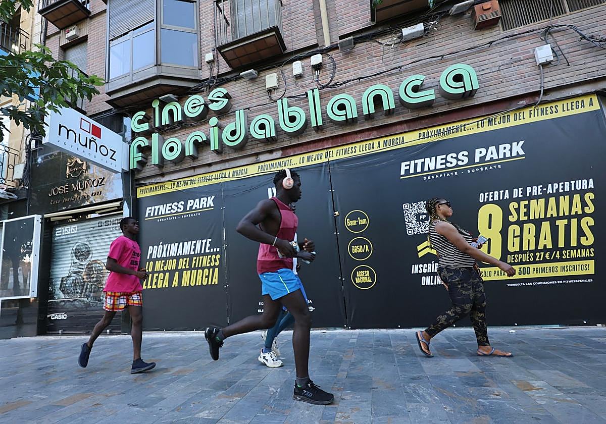 Viandantes y corredores pasan por delante de la lona que anuncia la apertura de un gimnasio en los antiguos Cines Floridablanca.