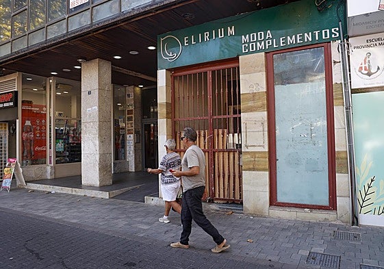 Dos personas caminan frente a la entrada del antiguo local comercial okupado.