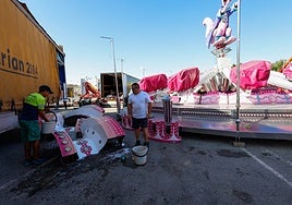 Feriantes limpian friegan las piezas del 'Canguro Loco' para su montaje en el Huerto de la Rueda.