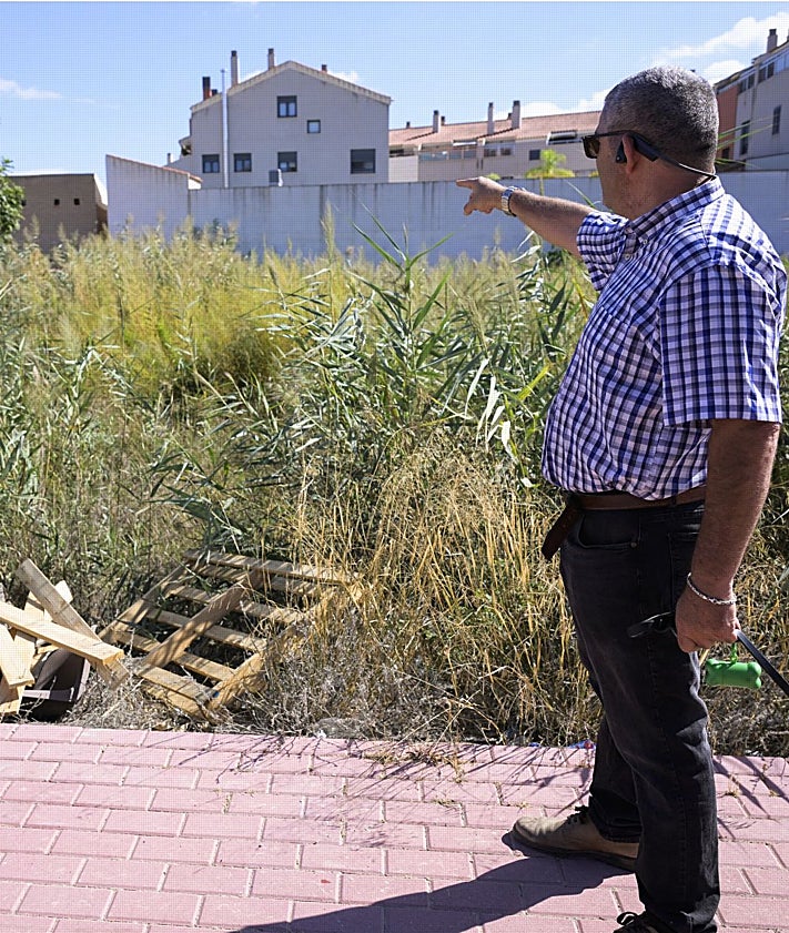 Imagen secundaria 2 - En la imagen superior, varios transeúntes pasan por delante de un tramo forzado de la valla perimetral. Abajo, detalle una zona central de la zona verde, con muestras de haber sido usada para pernoctar al raso. En la fotografía inferior, un vecino señala las casas vecinas cercanas a un entorno cubierto de malezas y con restos de palés de madera rotos.