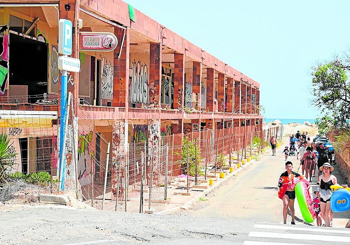 Grupos de bañistas pasan junto al edificio que será demolido, en la zona norte de La Manga.