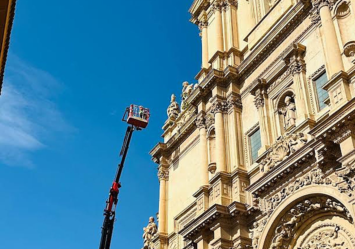Una camión grúa con cesta se acerca a la fachada de la antigua colegiata para la retirada de las plantas.