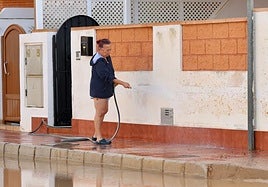 Una mujer limpia la calle, llena de barro tras las lluvias de la dana.