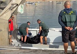Agentes de la Guardia Civil recuperan el cadáver hallado en el puerto pesquero de Águilas.