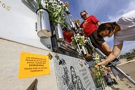 Una pareja poniendo flores junto a un nicho con cartel informativo, en el cementerio de Cabezo de Torres, este viernes por la mañana.