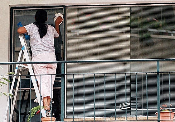 Una trabajadora del hogar limpia los cristales en una vivienda.